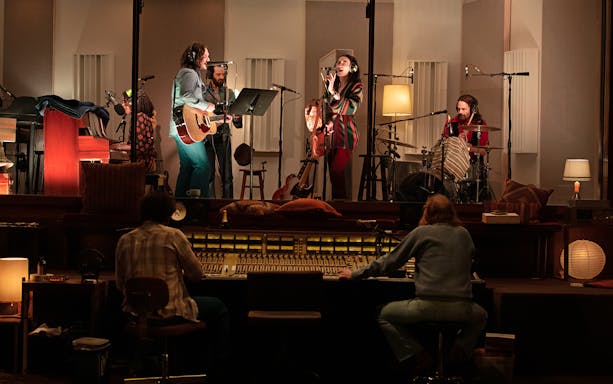 Musicians recording in a studio with guitars, drums, and sound equipment, related to Stereophonic.
