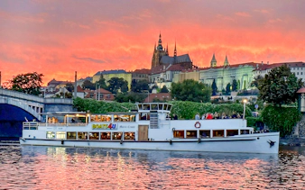 Cruise boat on Vltava River with Prague Castle at sunset.
