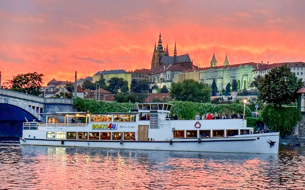 Cruise boat on Vltava River with Prague Castle at sunset.