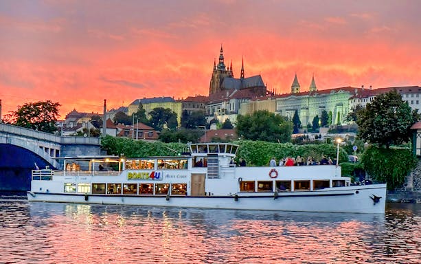 Cruise boat on Vltava River with Prague Castle at sunset.