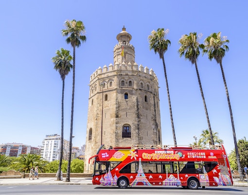 Tourists exploring Seville on a Hop-On Hop-Off Bus Tour with a view of the Alcazar of Seville, a unique combo deal saving 5%