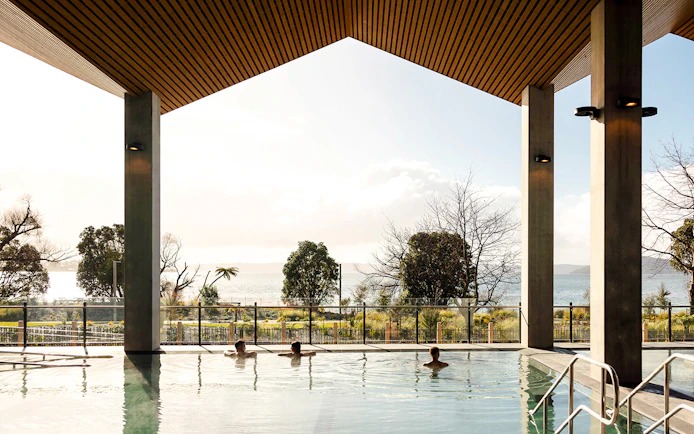 Wai Ariki Hot Springs & Spa indoor pool with lake view and visitors relaxing.