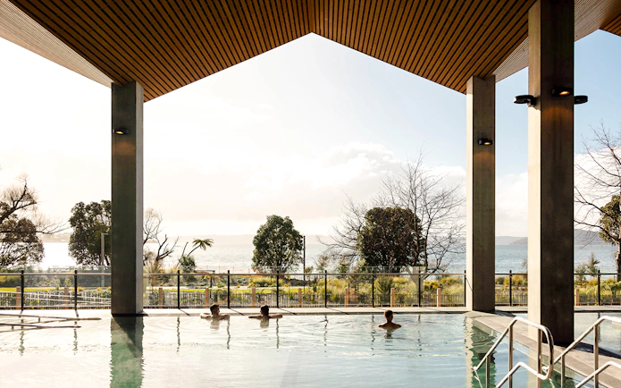 Wai Ariki Hot Springs & Spa indoor pool with lake view and visitors relaxing.