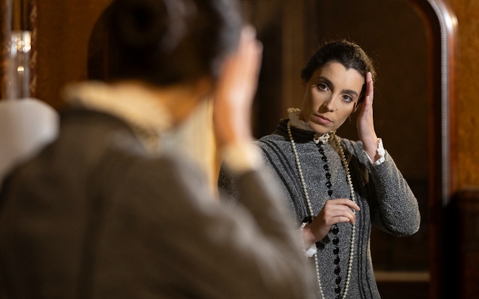 Woman in period costume adjusting hair in front of a mirror at the Palace of Pena, Portugal.