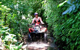 Young woman quad biking through lush jungle trail in Bali.