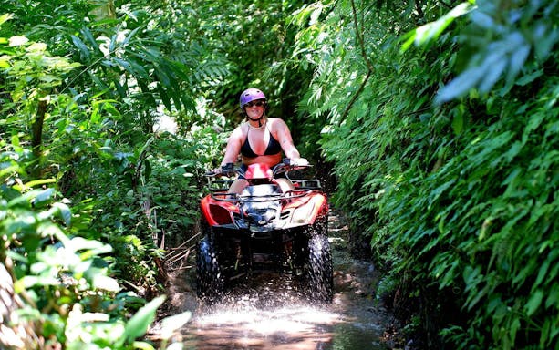 Young woman quad biking through lush jungle trail in Bali.