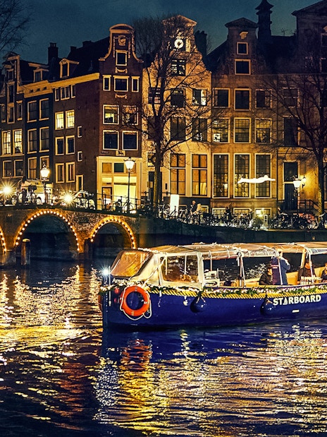 Small-group cruise on Amsterdam canal during Light Festival with illuminated art and historic buildings.