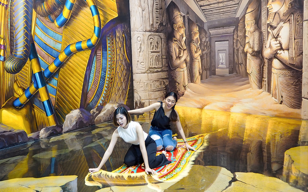 Two visitors on a 3D magic carpet illusion at Art in Paradise Pattaya, with Egyptian-themed murals.