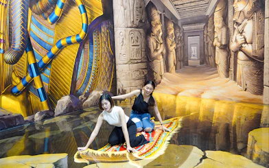 Two visitors on a 3D magic carpet illusion at Art in Paradise Pattaya, with Egyptian-themed murals.