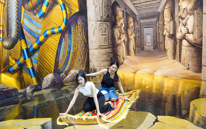 Two visitors on a 3D magic carpet illusion at Art in Paradise Pattaya, with Egyptian-themed murals.