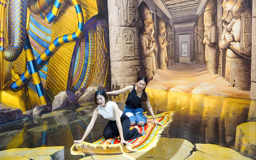 Two visitors on a 3D magic carpet illusion at Art in Paradise Pattaya, with Egyptian-themed murals.