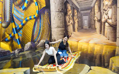 Two visitors on a 3D magic carpet illusion at Art in Paradise Pattaya, with Egyptian-themed murals.