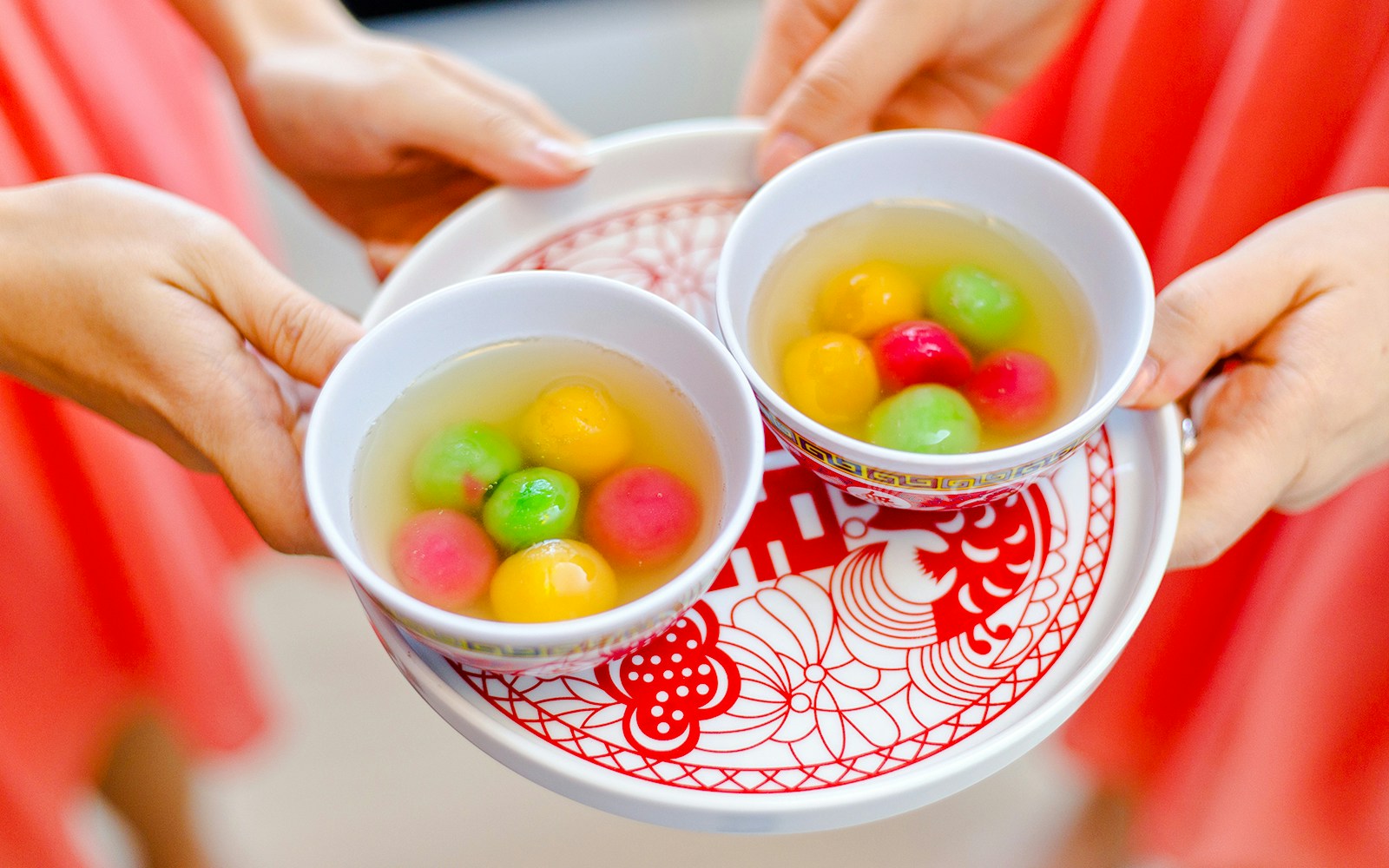 Bowls of colorful Tang Yuan in sweet syrup on a decorative tray.