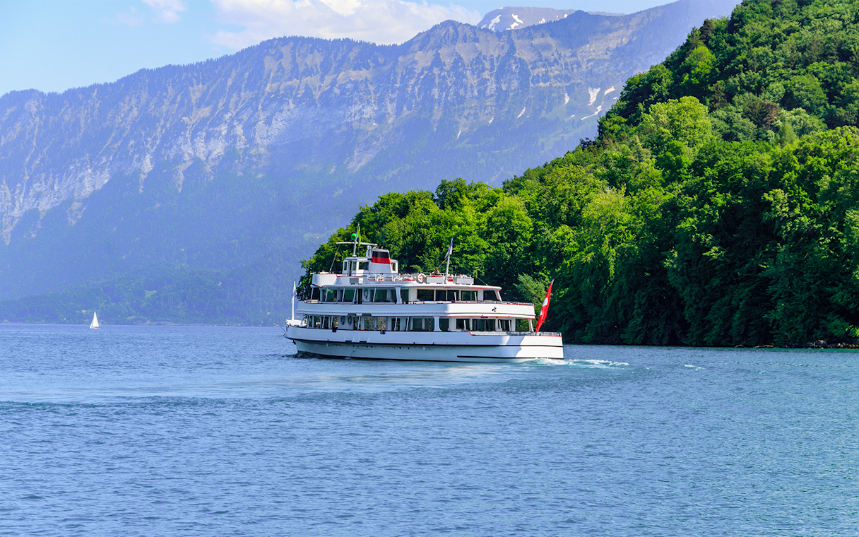 Passenger ship cruising on Lake Thun, Switzerland, with mountains in the background.