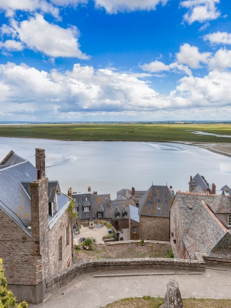 Rooftops of Mont St. Michel overlooking tidal flats and sea, seen on a full day tour from Paris.