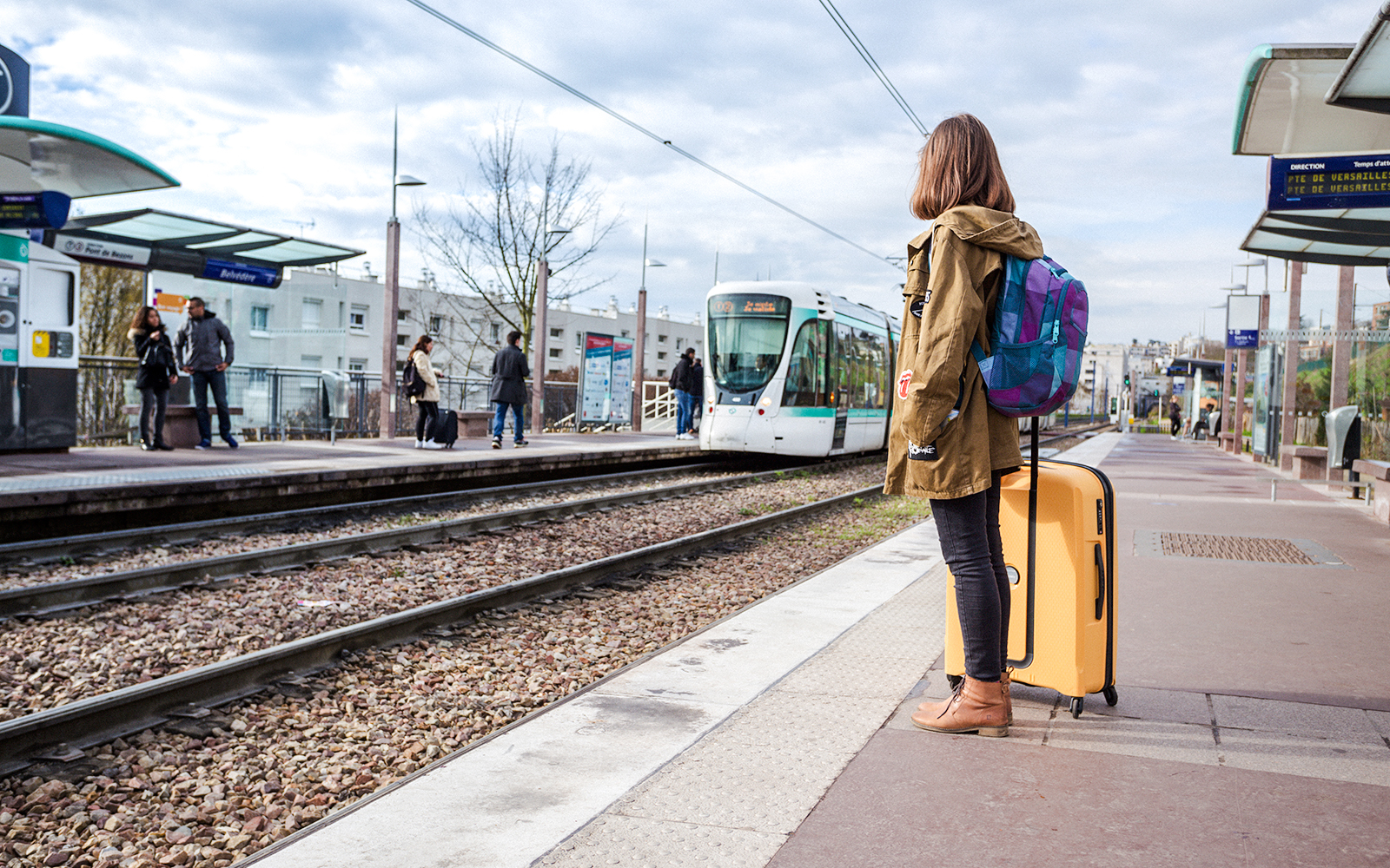 Traveler waiting at Chenonceaux station with luggage and tram approaching.