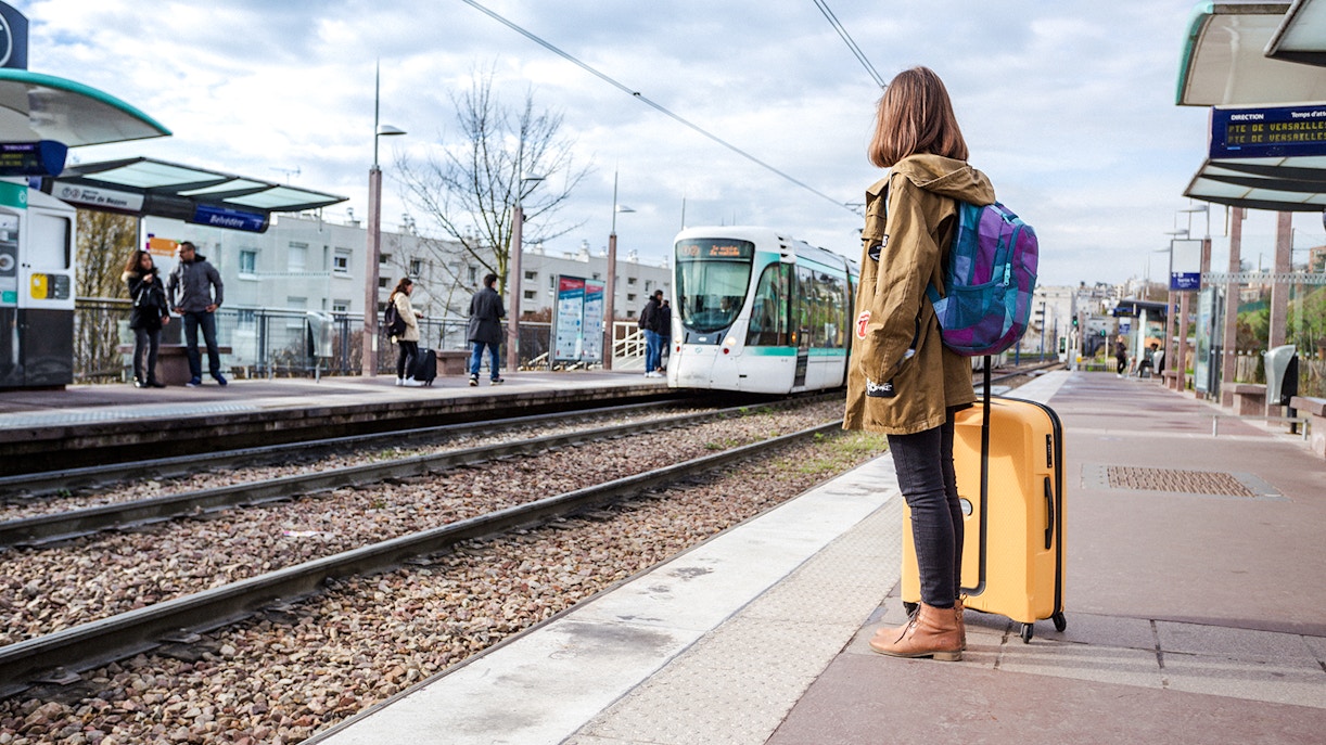 Traveler waiting at Chenonceaux station with luggage and tram approaching.