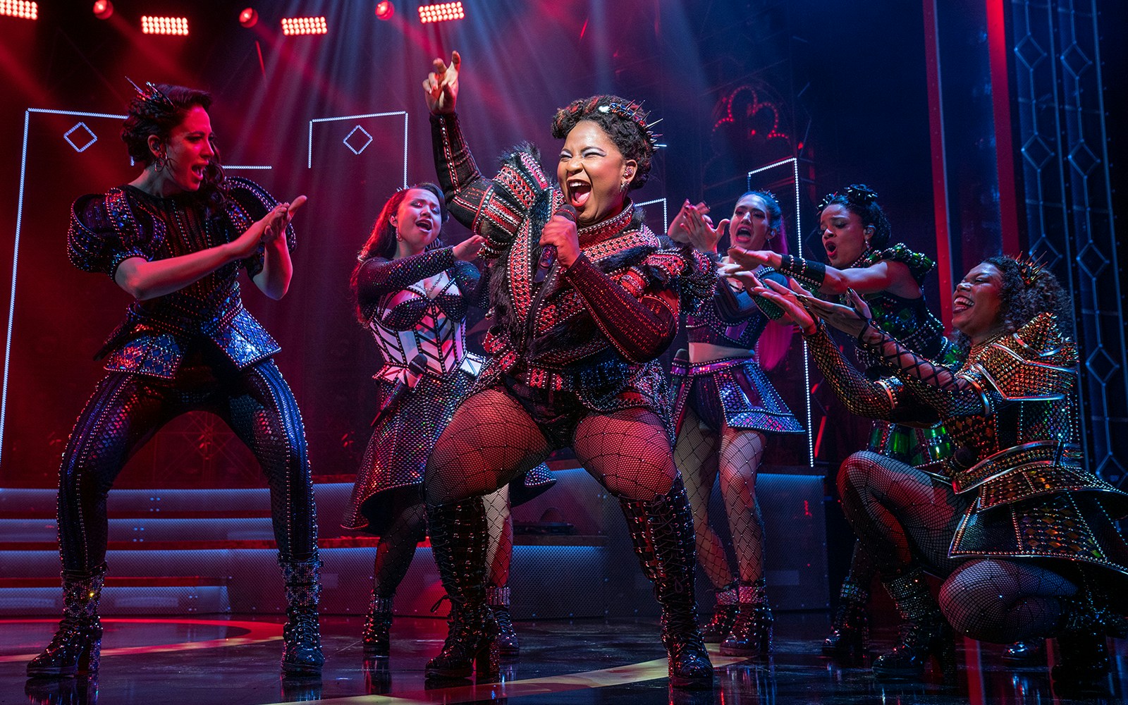 Performers in vibrant costumes singing on stage during SIX: The Musical.