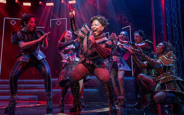 Performers in vibrant costumes singing on stage during SIX: The Musical.