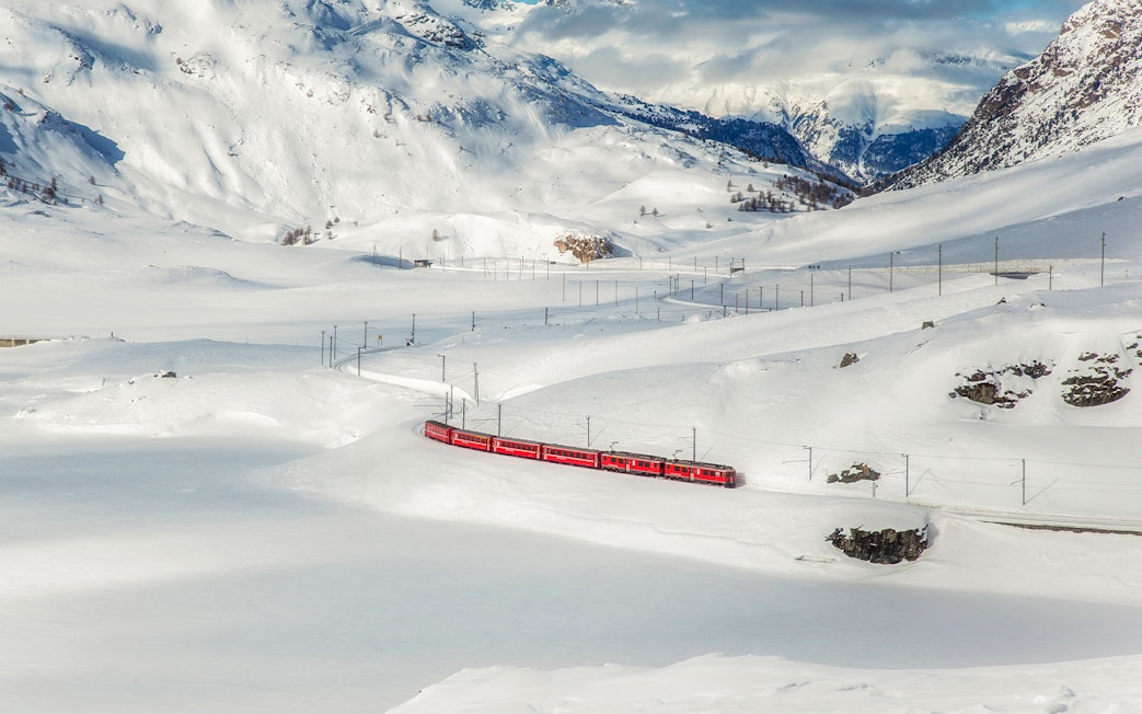 Bernina train traveling through snowy Swiss Alps landscape.