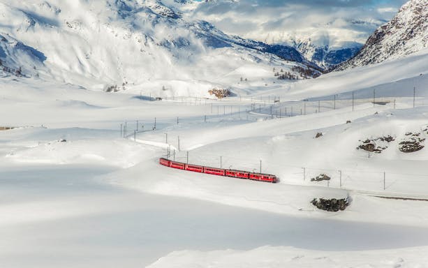Bernina train traveling through snowy Swiss Alps landscape.