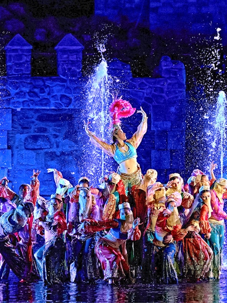 Performers in colorful costumes during The Dream of Toledo Night Show with fountains in the background.