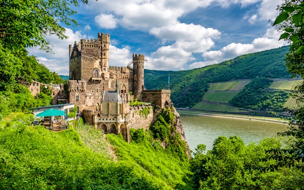 Rheinstein Castle overlooking the Rhine River in Rhine Valley, surrounded by lush greenery.