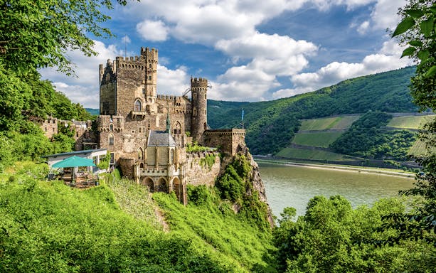 Rheinstein Castle overlooking the Rhine River in Rhine Valley, surrounded by lush greenery.