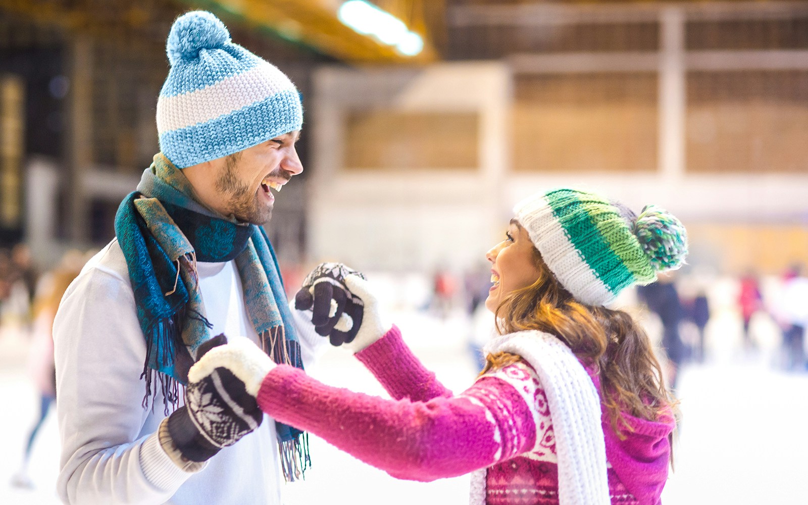 Young couple laughing while ice skating indoors.