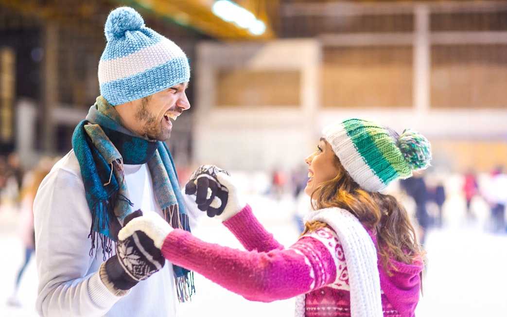 Young couple laughing while ice skating indoors.