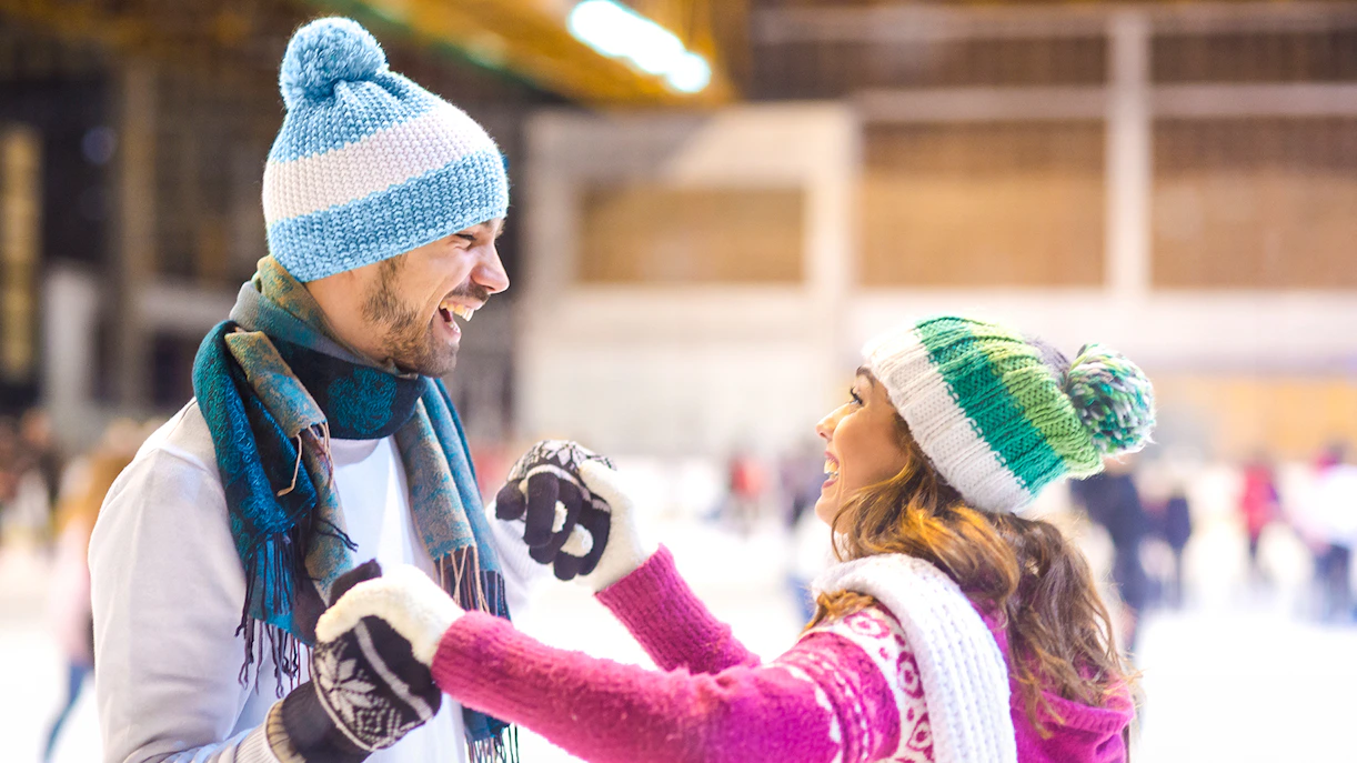 Young couple laughing while ice skating indoors.