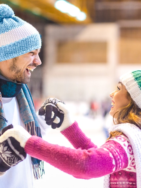 Young couple laughing while ice skating indoors.
