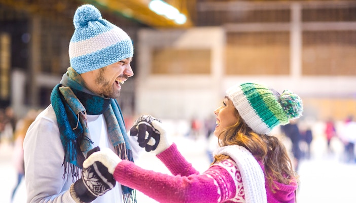 Young couple laughing while ice skating indoors.