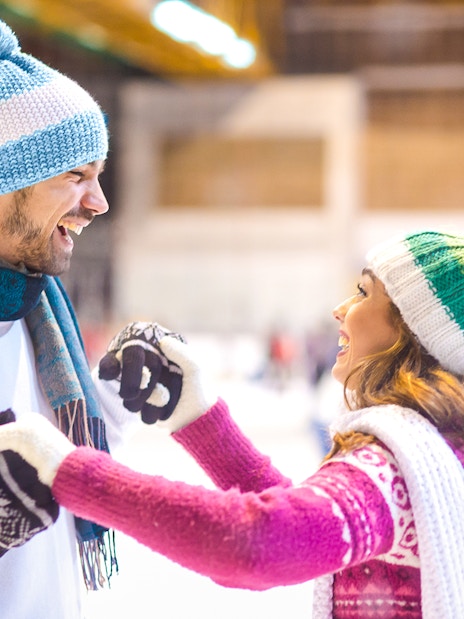 Young couple laughing while ice skating indoors.