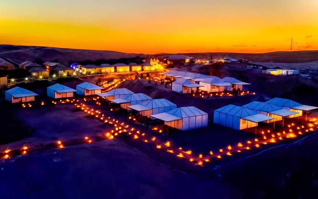 Marrakech Agafay desert camp illuminated at night with tents and lanterns.