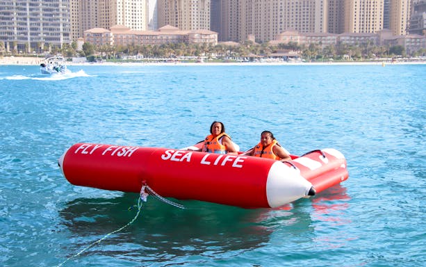 Two people on a Fly Fish inflatable ride in Dubai Marina waters.