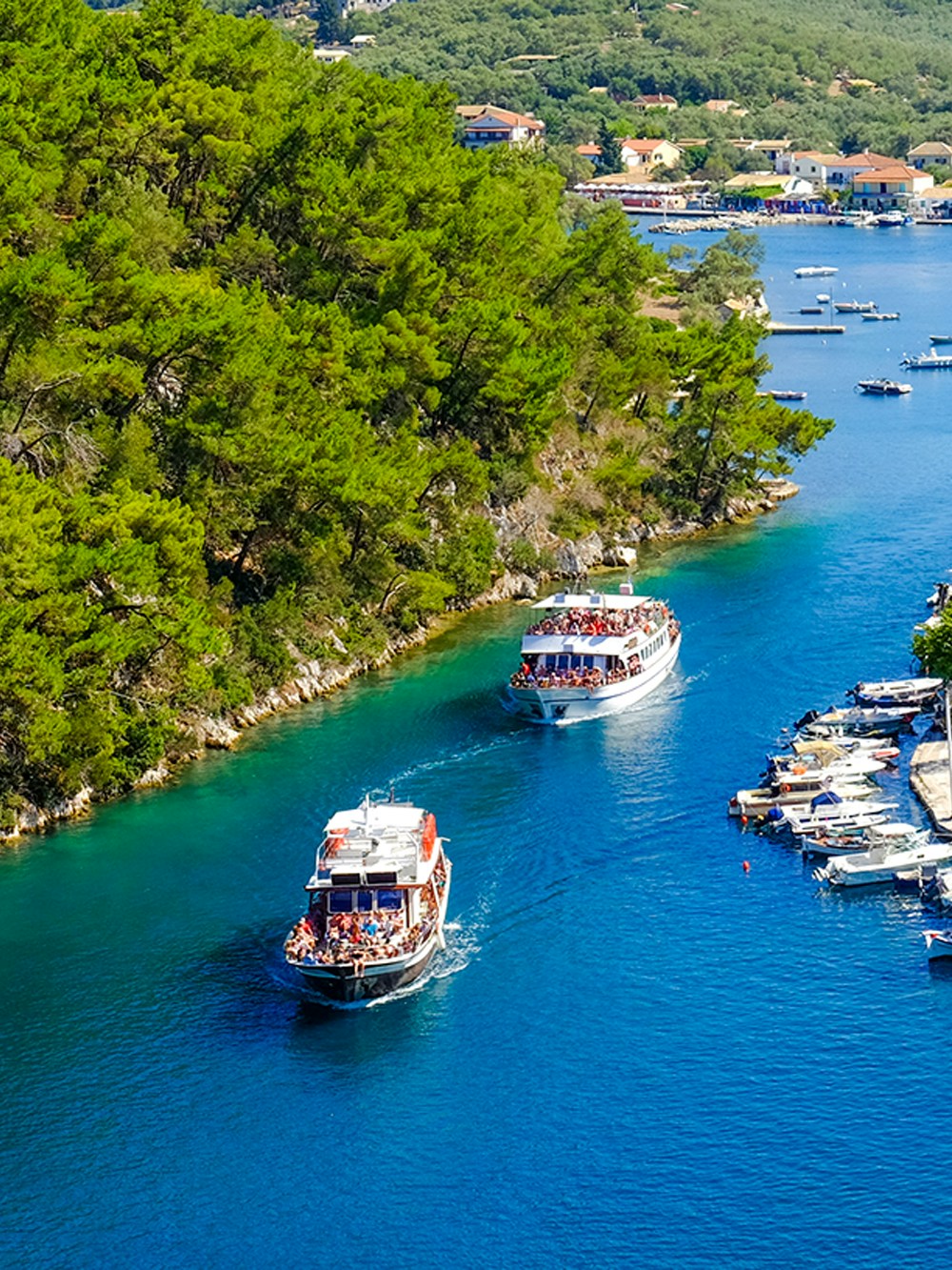 Boats navigating the canal on Paxos Island, Greece, surrounded by lush greenery.