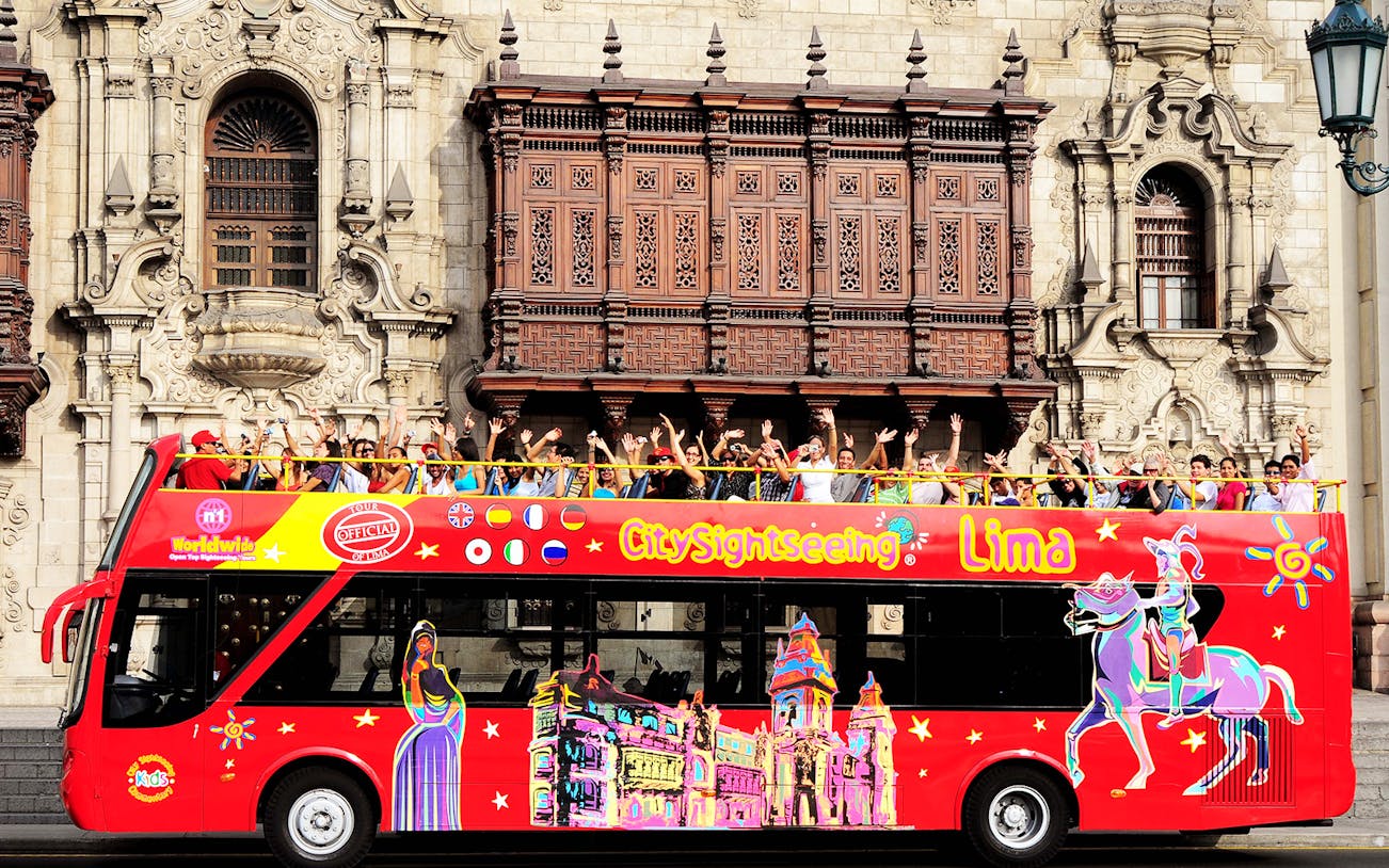 Open-top sightseeing bus in Lima, Peru, with tourists in front of historic architecture.