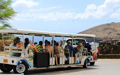 Tourists on a tram at Hanauma Bay Nature Preserve with ocean and cliffs in the background.