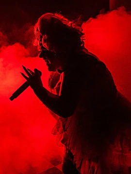 Performer singing at Madame Arthur Show in Paris, surrounded by red stage lighting.