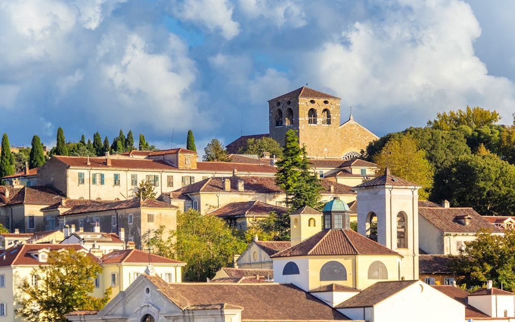 Historic buildings on San Giusto Hill, Trieste, with a church tower and lush greenery.