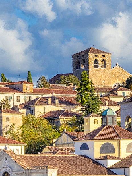 Historic buildings on San Giusto Hill, Trieste, with a church tower and lush greenery.