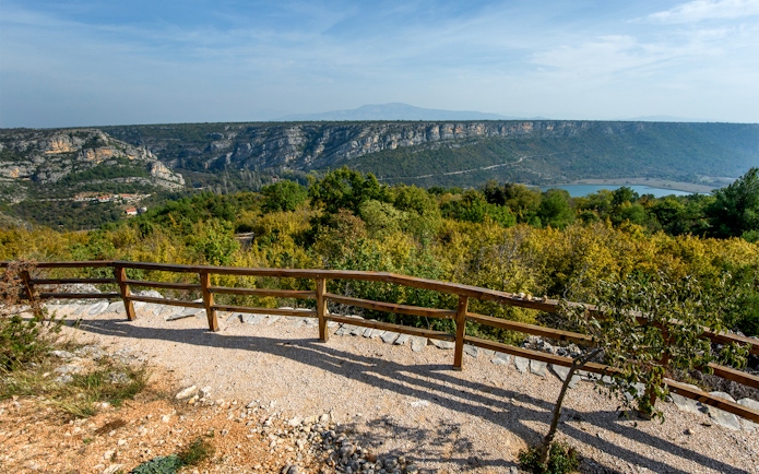 View from a wooden railing at Krka National Park overlooking lush greenery and distant cliffs.
