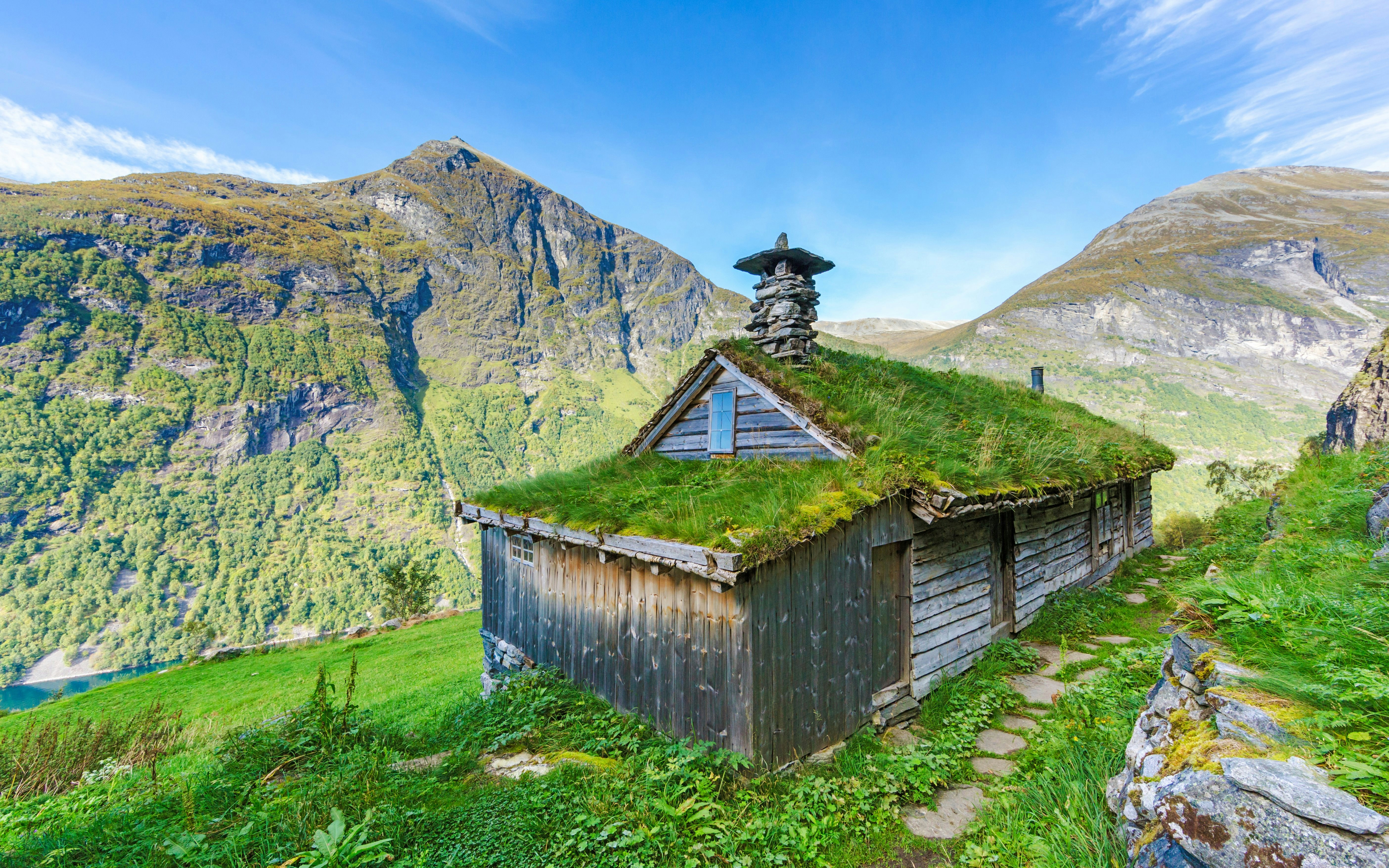 Skagefla hut with grass roof overlooking Geiranger fjord, Norway, surrounded by mountains.