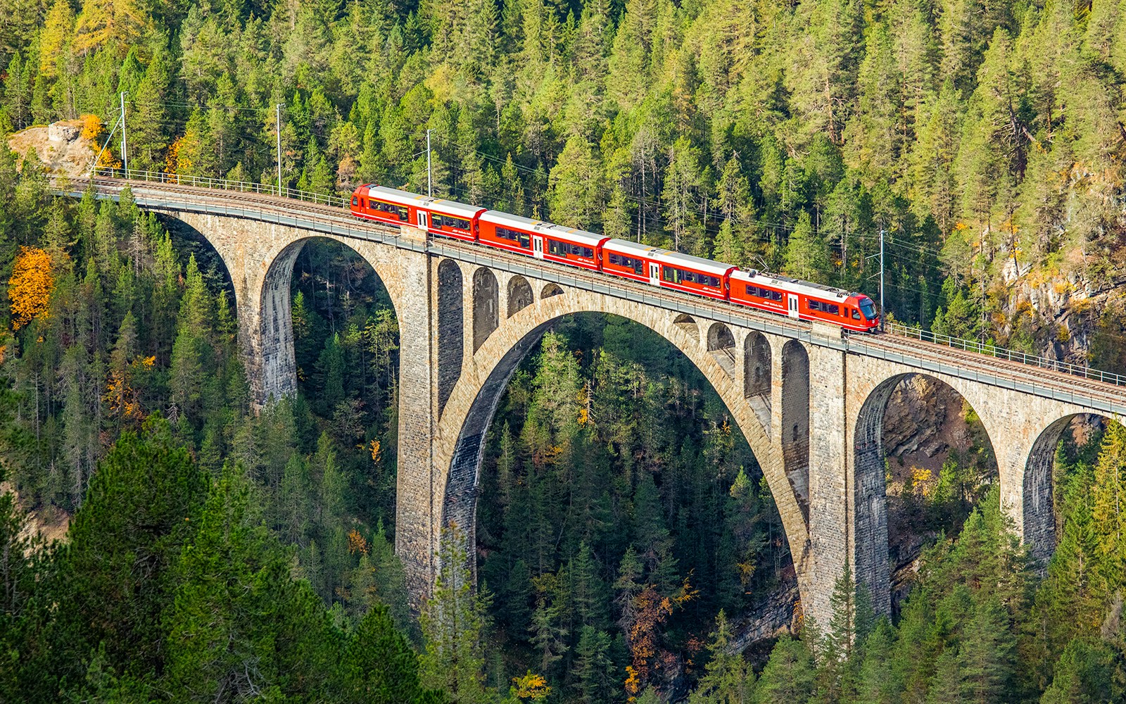 A red passenger train is crossing the famous Wiesener viaduct on the train line Davos - Filisur, the highest viaduct in swiss alps