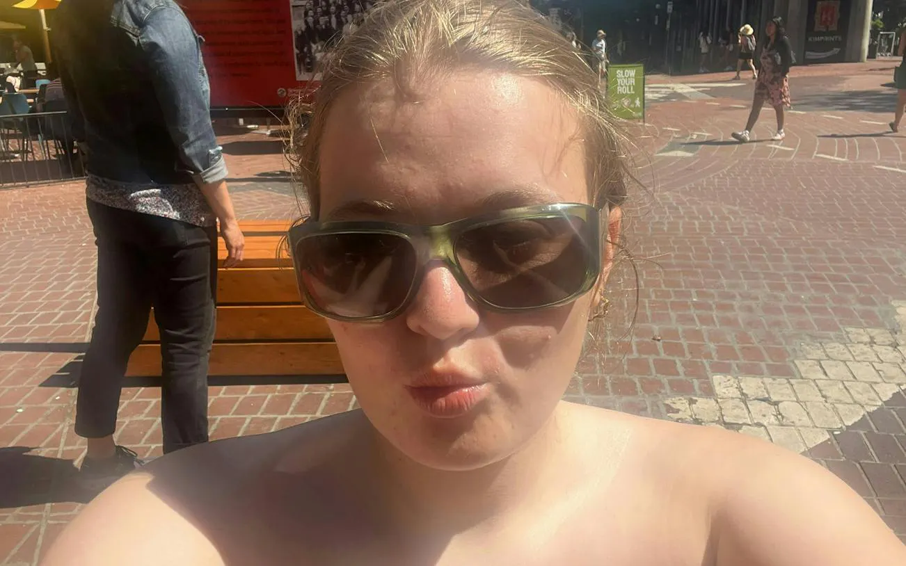 A person wearing sunglasses in Vancouver's Gastown, with cobblestone streets and pedestrians in the background.