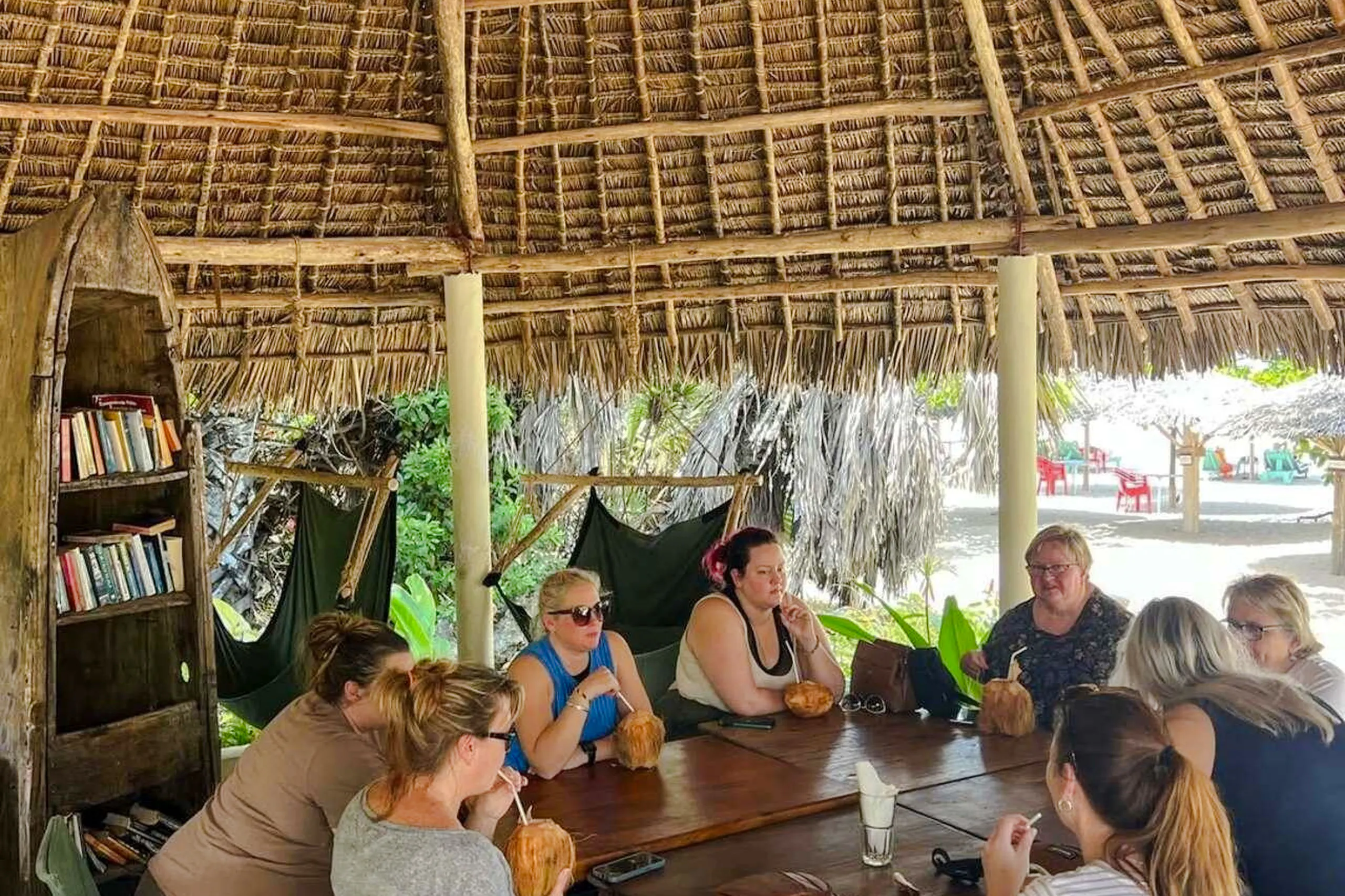 Group enjoying drinks under a thatched pavilion at a Zanzibar beach resort.