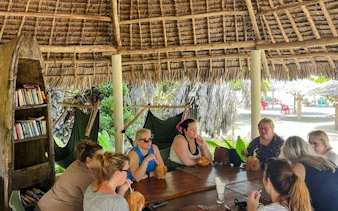 Group enjoying drinks under a thatched pavilion at a Zanzibar beach resort.