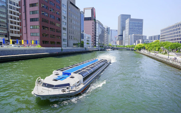 River cruise boat on Osaka canal with city skyline, part of Osaka Amazing Pass experience.