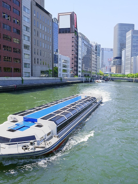 River cruise boat on Osaka canal with city skyline, part of Osaka Amazing Pass experience.